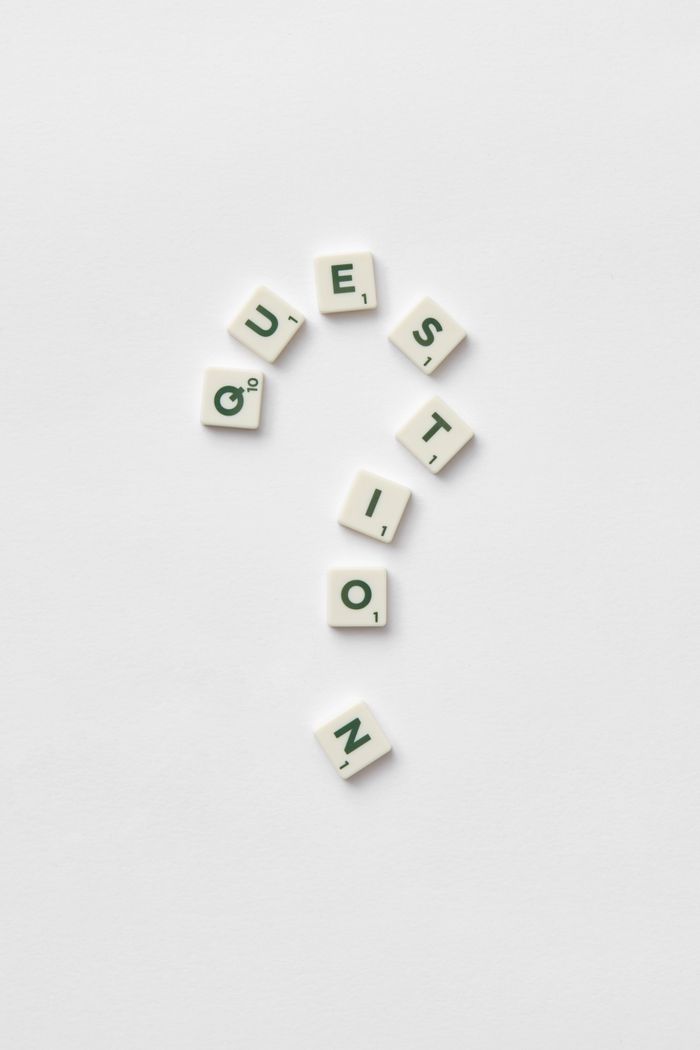 Artistic arrangement of letter tiles forming a question mark on a white background.