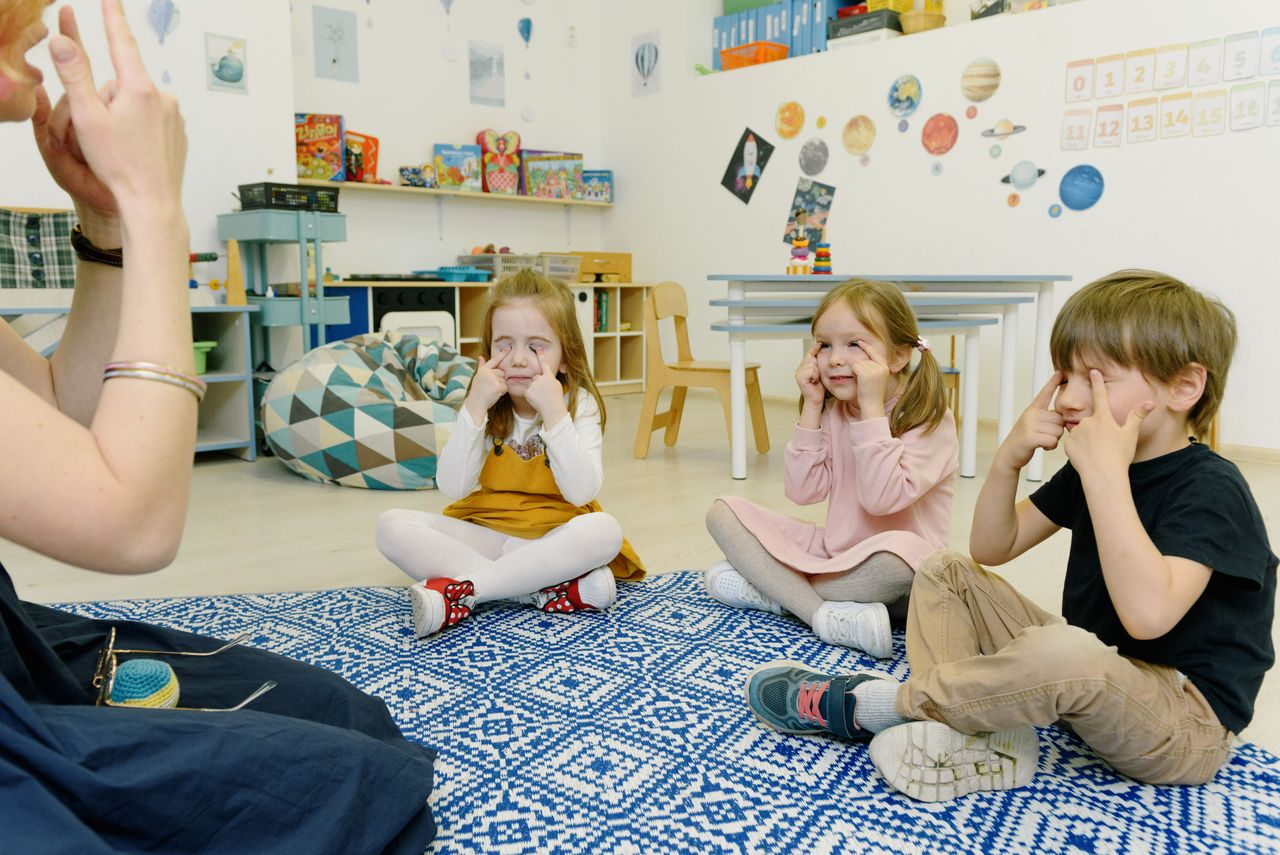 Group of children in a kindergarten class with tutor, playing and learning in a colorful room.